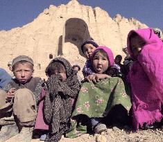 Afghan children, who live a stone cave at Bamian, Afghanistan pose to a camera.  The back scene stands the ruins of Great Buddha image